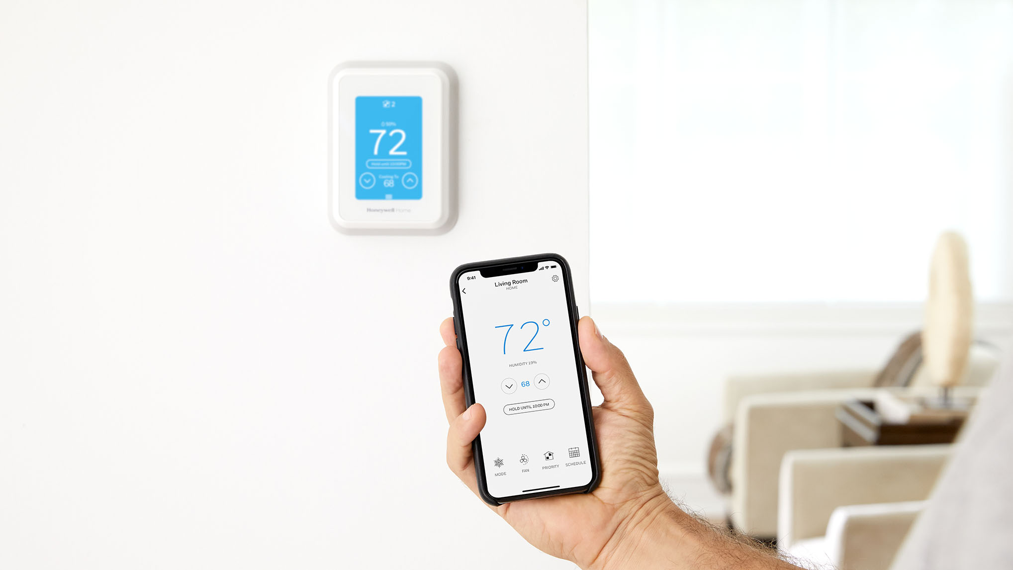 Thermostat on a wall and hand holding a phone with a thermostat app that shows with matching temperatures