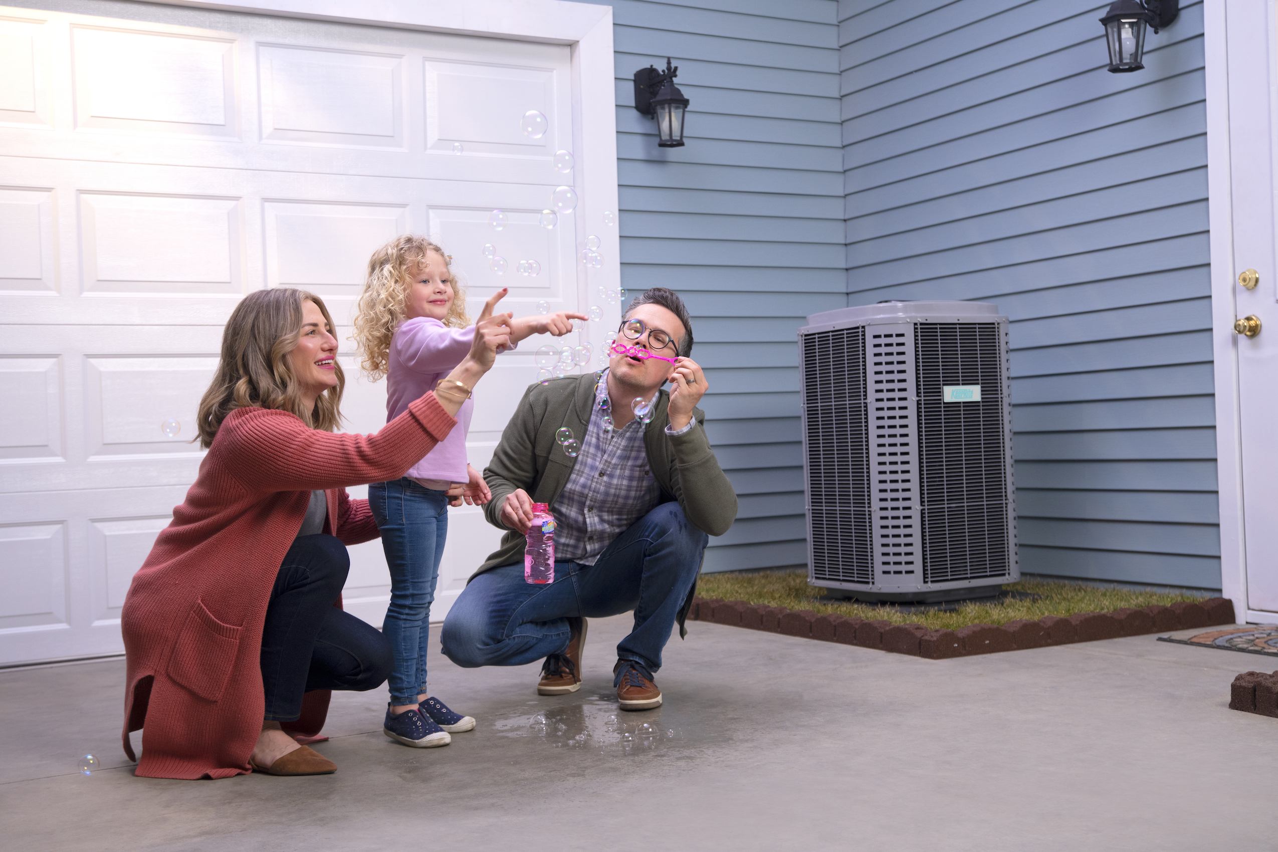 Family blowing bubbles outside next to an air conditioner unit