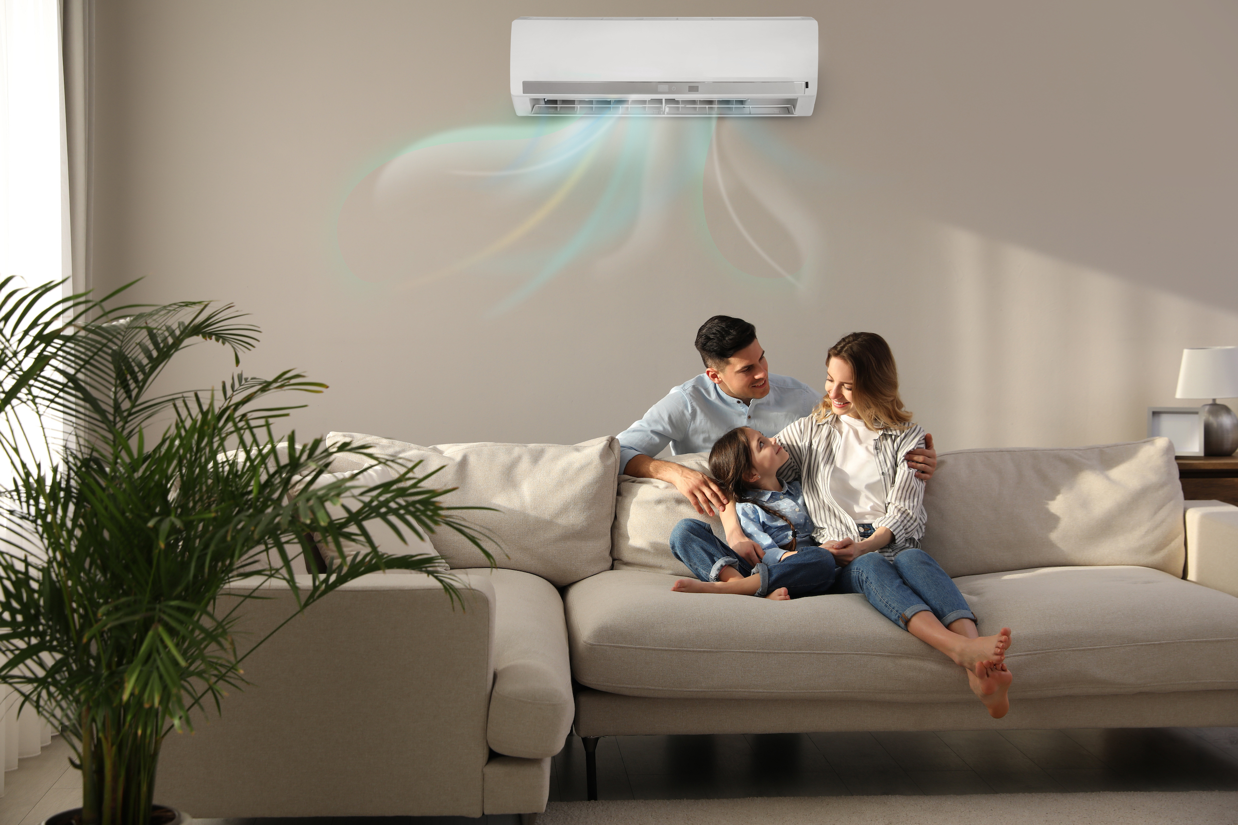 Family sitting on a couch inside, with an indoor heat pump unit above them.